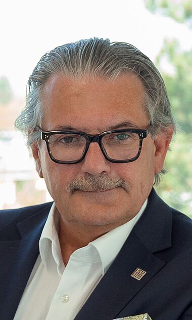 Ein Mann im Anzug lächelt freundlich in die Kamera.