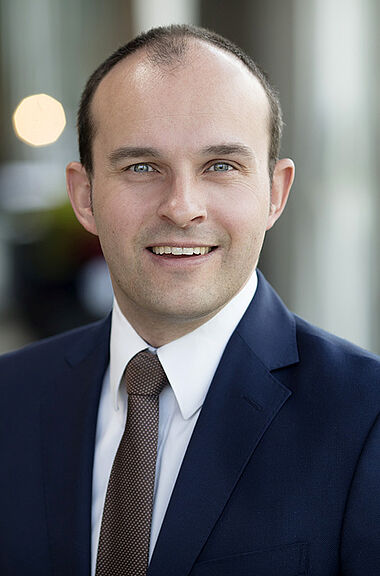 Ein Mann im Anzug lächelt professionell in die Kamera.