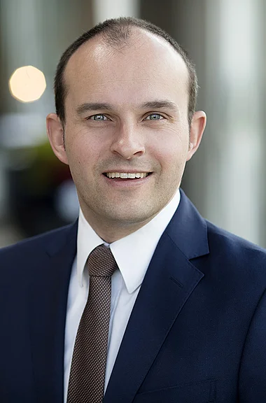 Ein Mann im Anzug lächelt professionell in die Kamera.