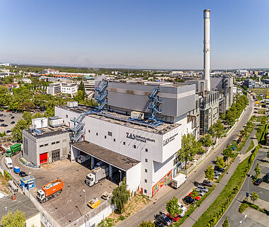 Industrieanlage mit Kamin und Logistikbereich, aufgenommen aus der Vogelperspektive.