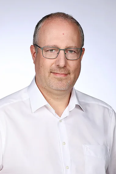 Porträt eines Mannes mit Brille und weißem Hemd.