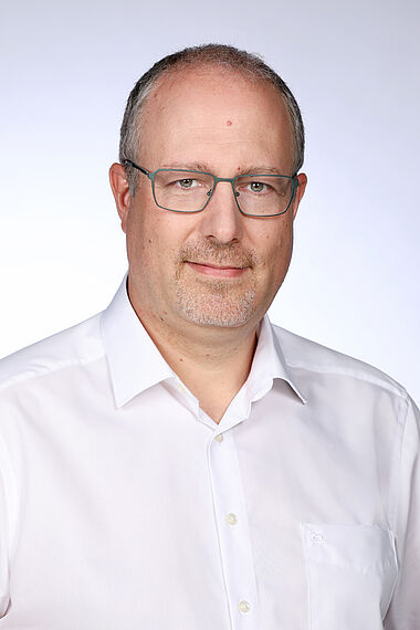 Porträt eines Mannes mit Brille und weißem Hemd.