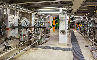 Technikraum mit Rohrleitungen, Ventilen und Bedienelementen für industrielle Prozesse.