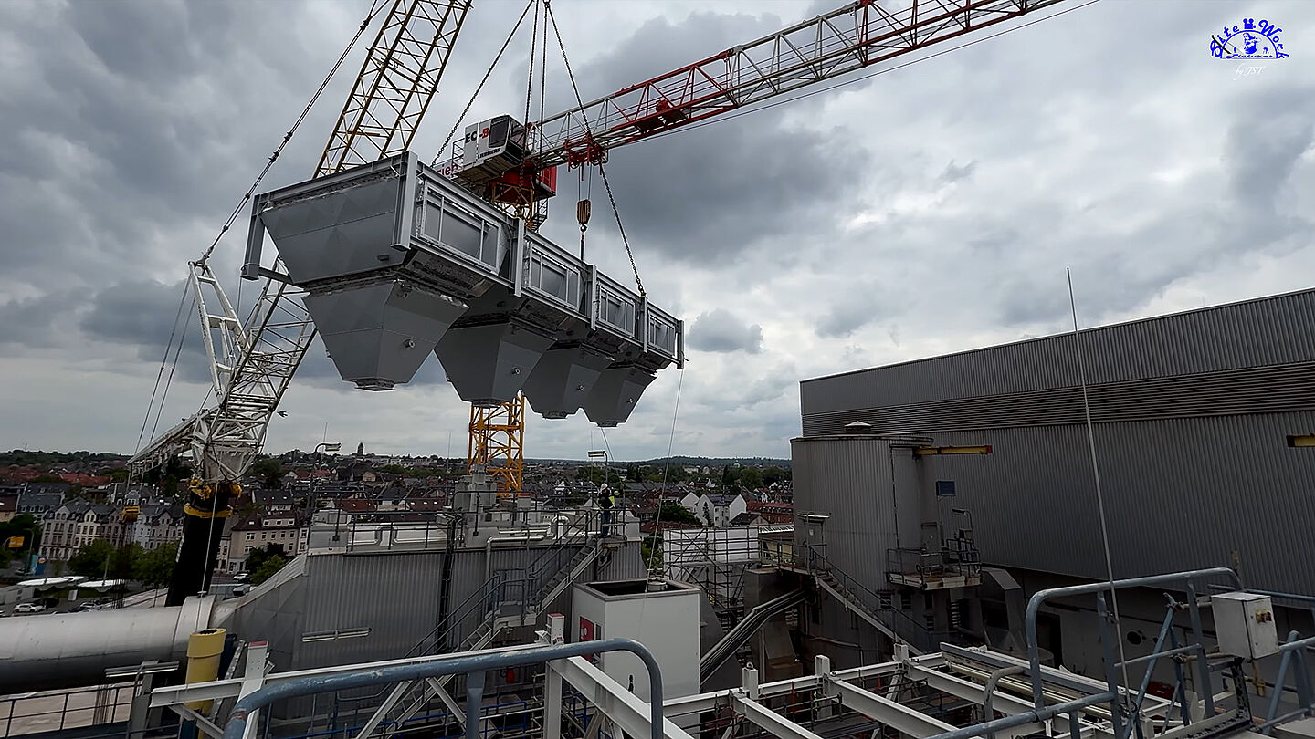 Kran hebt eine große Anlage vor städtischer Kulisse.