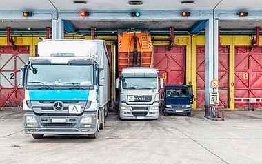 Drei Lastkraftwagen stehen nebeneinander vor einer Lagerhalle.