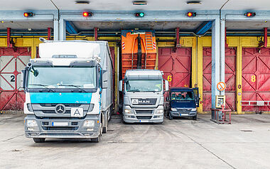 Drei Lastkraftwagen stehen nebeneinander vor einer Lagerhalle.