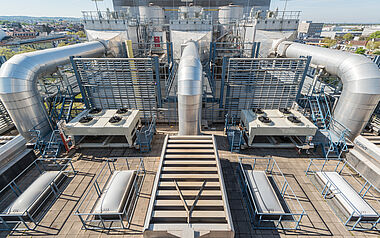 Technische Anlage mit Lüftungsrohren und Kühler auf einem Flachdach.